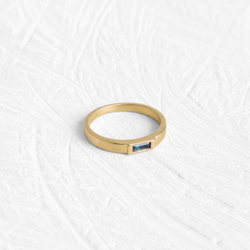This sleek ring has a flattened bezel that is almost flush with the band and is set with a sapphire.