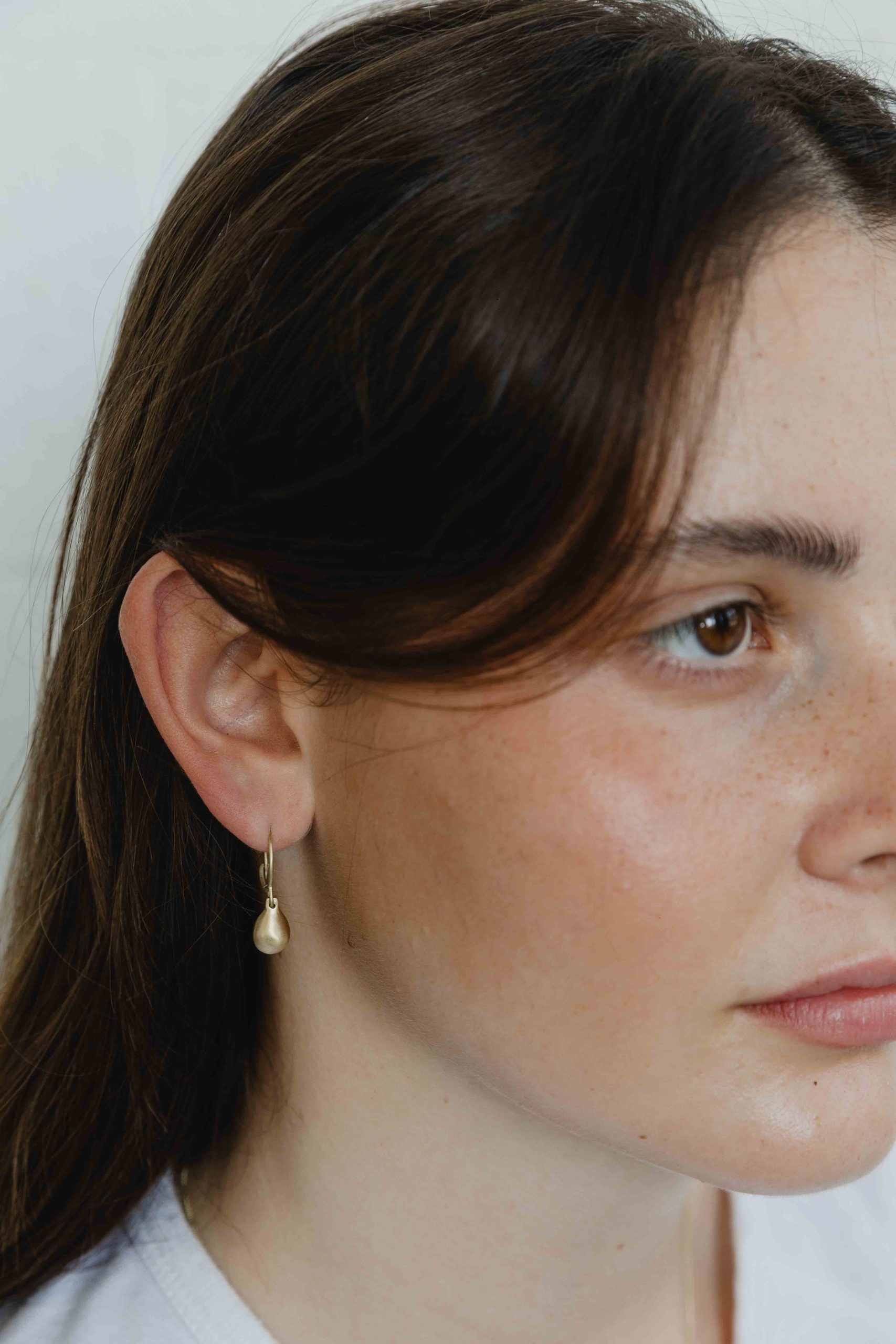 Golden hoops earrings with a dangling golden pear shaped element. A contemporary, minimalist and ... - View 3