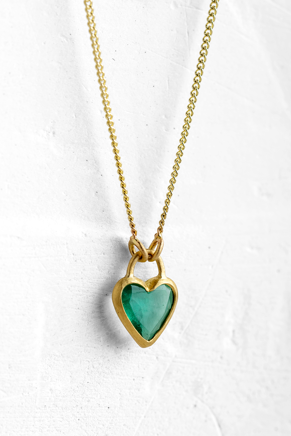 A handmade pendant is set with a Green Emerald in a heart shape which hangs on a delicate chain