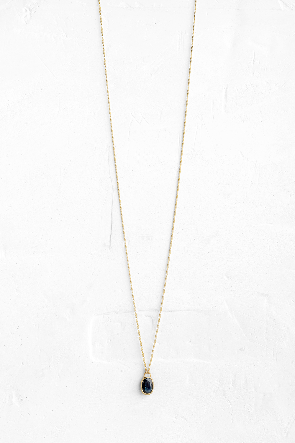 A handmade pendant is set with a deep Blue Saphire stone which hangs on a delicate chain - View 2