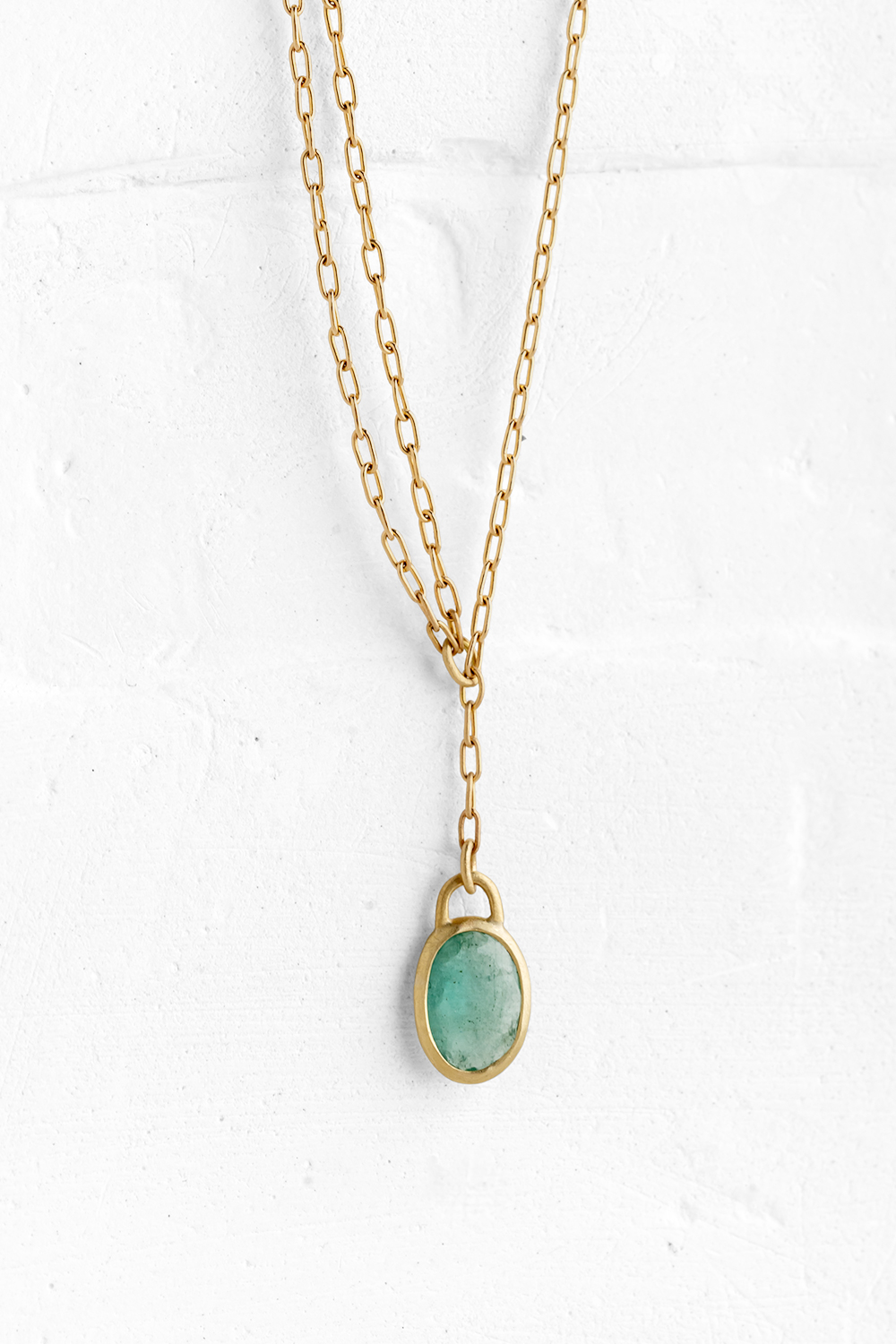 A handmade pendant is set with an oval one of a kind Emerald stone which hangs on a delicate chain