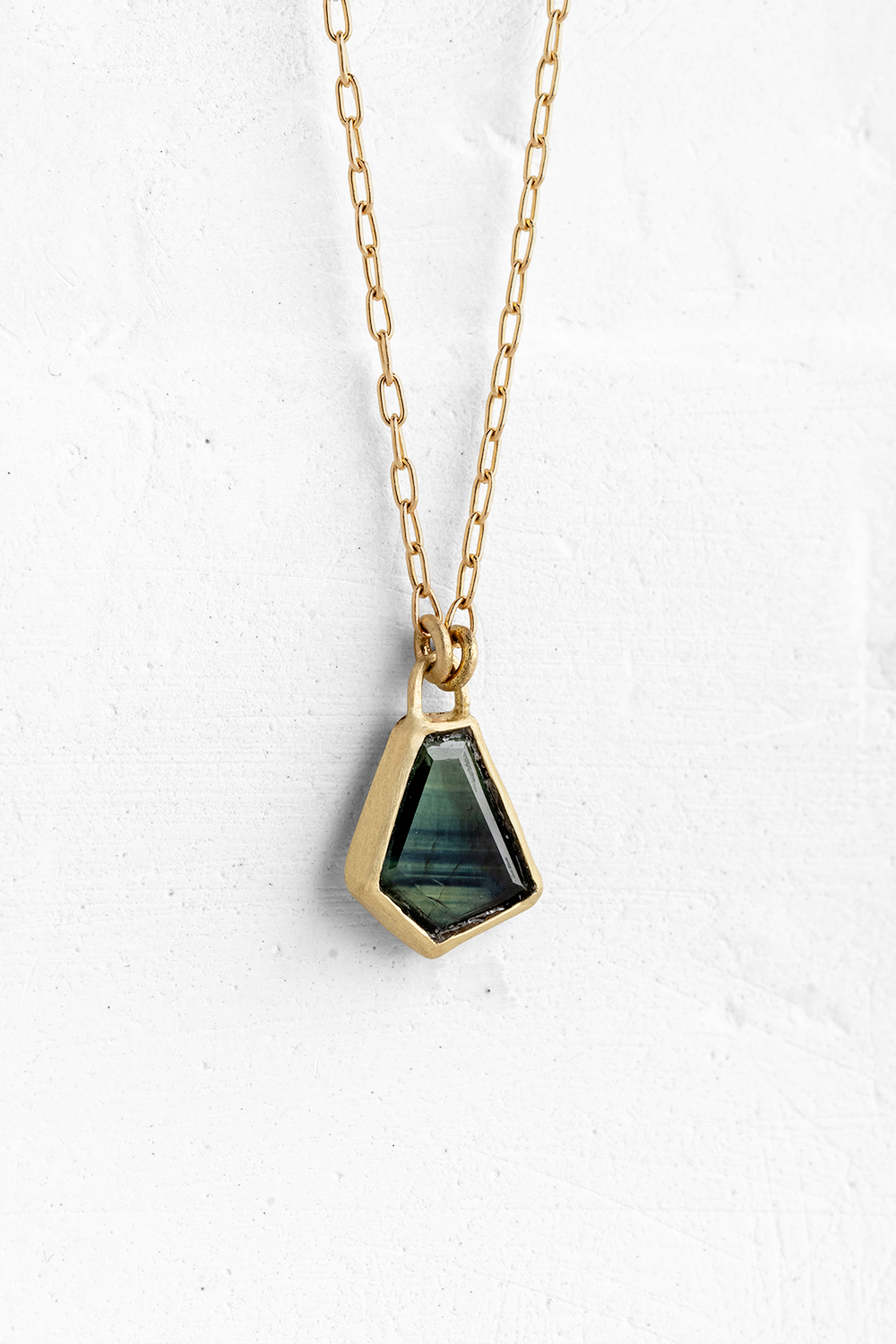A handmade pendant set with a beautiful amorphous shaped Green Sapphire hanging on a delicate gol...