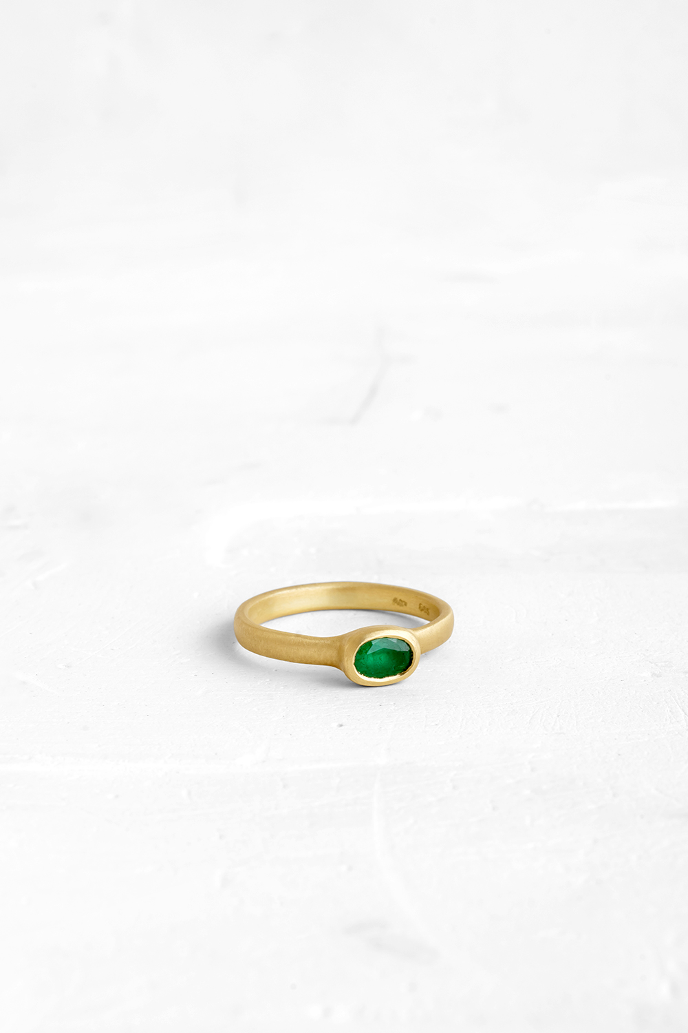 The band and the bezel are both crafted into one fluid piece in this ring and set with an Emerald
