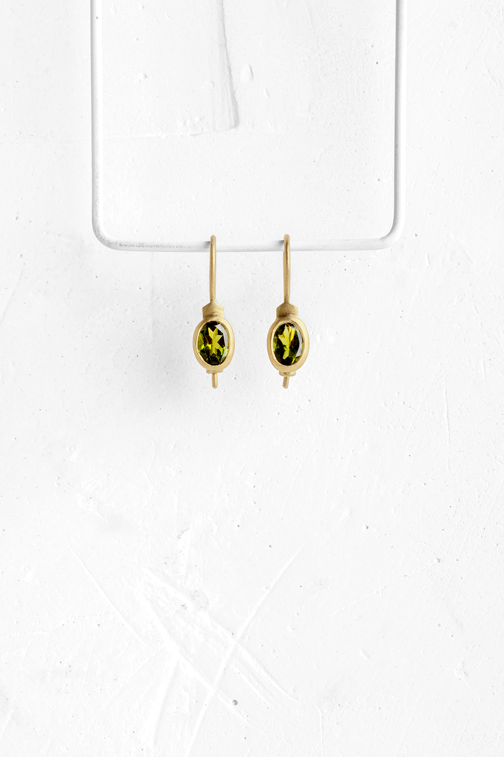These elegant hanging earrings are set with oval Green Tourmaline stones & wrapped in 18K gold
