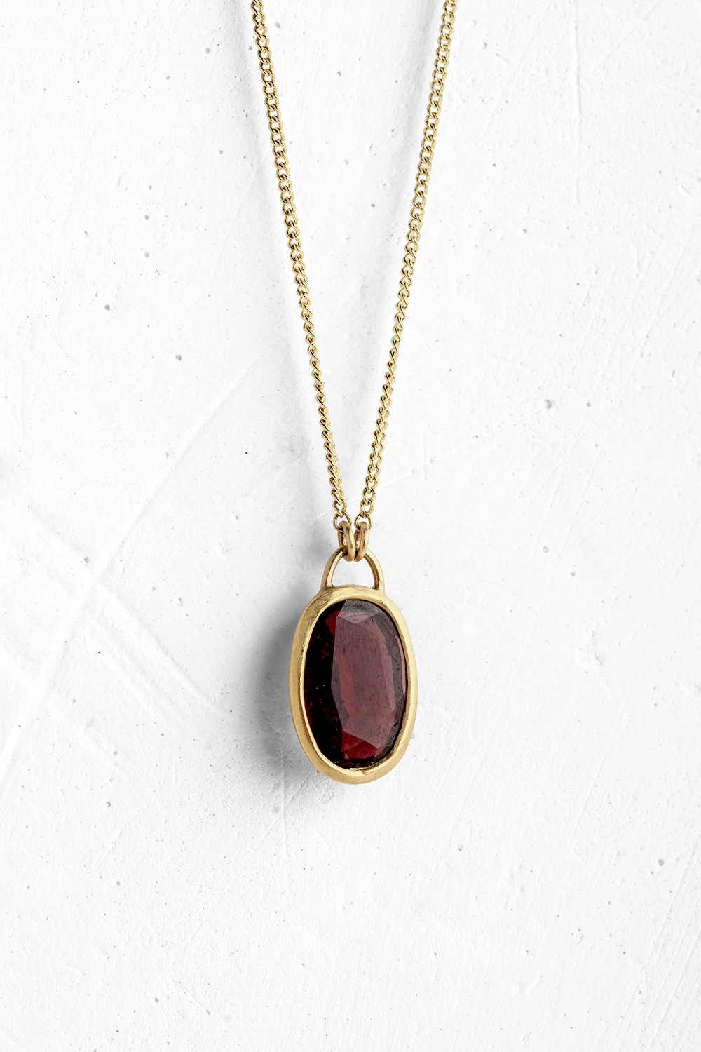 A handmade pendant is set with a deep pink Rhodolite stone which hangs on a delicate chain